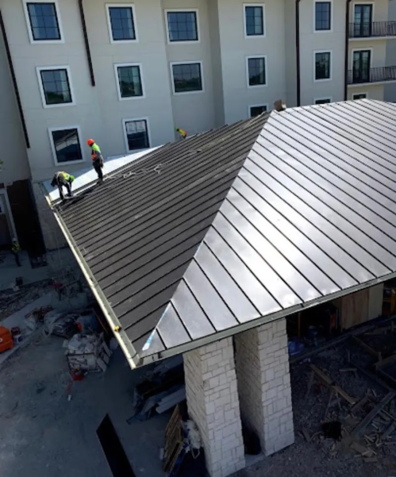 Crew installing standing seam metal roof panels on a commercial project in Allen